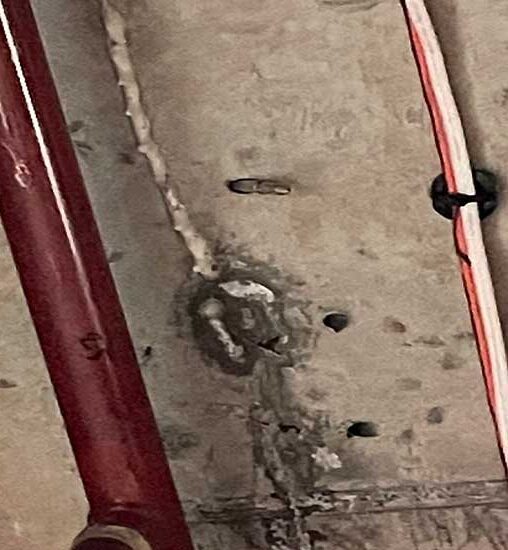 Concrete ceiling with visible cracks and drilled holes near service pipes, requiring structural inspection and repair